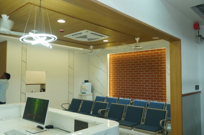 The reception lobby: a backlit brick feature wall, a ring chandelier over the desk and a row of blue waiting chairs.