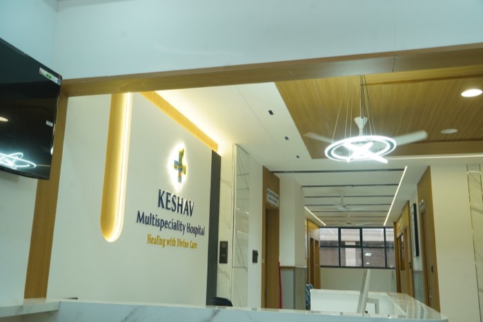 The wide reception area, with the illuminated Keshav logo wall and a warm wood-slat ceiling above the desk.