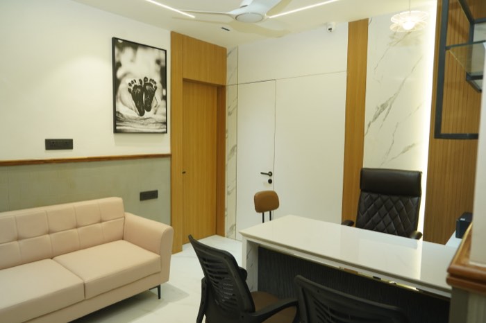 A consulting room with a cream sofa, a marble-topped desk and a framed black-and-white photograph of a newborn’s feet.