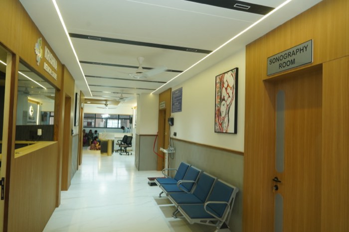 A long warmly lit corridor lined in teak, with the Krishna Medical Store counter on the left and the Sonography Room door on the right.