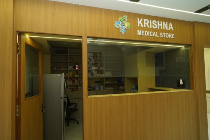 The Krishna Medical Store frontage: a teak-panelled pharmacy counter with a glazed window and stocked shelves behind.