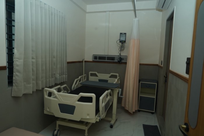 A private patient room with an adjustable bed, a bedside monitor, a curtain rail and a curtained window.