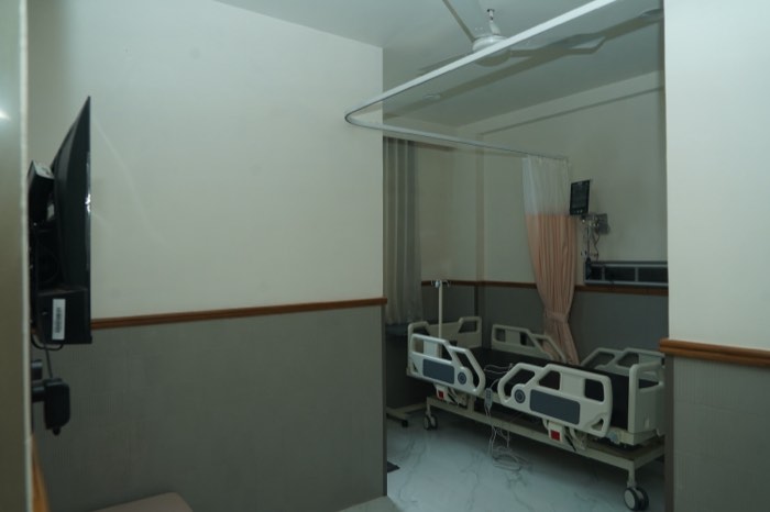 A twin-sharing room with two beds, a wall-mounted television and daylight from a side window.