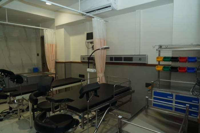 The labour room, with two delivery tables, blush curtains on ceiling rails and colour-coded supply bins along the wall.