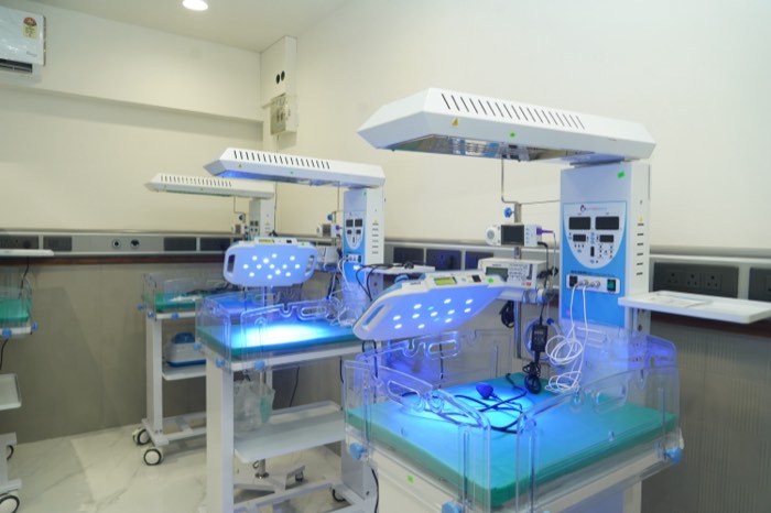 A close view of neonatal phototherapy units, their blue lamps lit above clear incubator hoods.