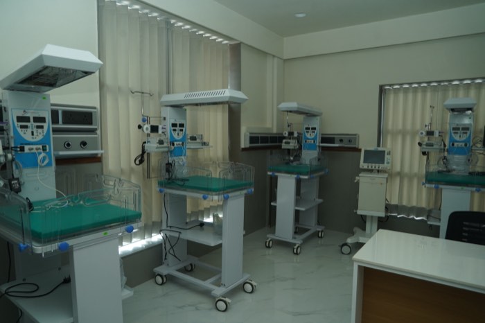 A row of neonatal radiant warmers with teal mattresses and monitoring equipment, ready and empty.